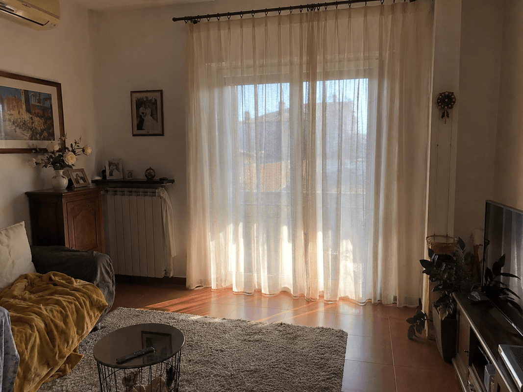 Tenda in tessuto naturale color beige burro su una grande finestra di un soggiorno luminoso, toni caldi 2026