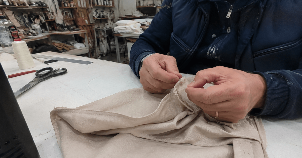 Mani di un tappezziere al lavoro su una fodera in laboratorio, vecchio tessuto e nuovo a confronto con ago e filo