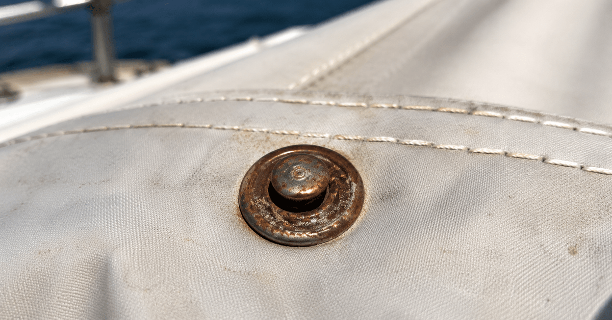 Dettaglio macro di bottoni automatici su un telo nautico, uno ossidato e grippato accanto a uno in acciaio inox lucido