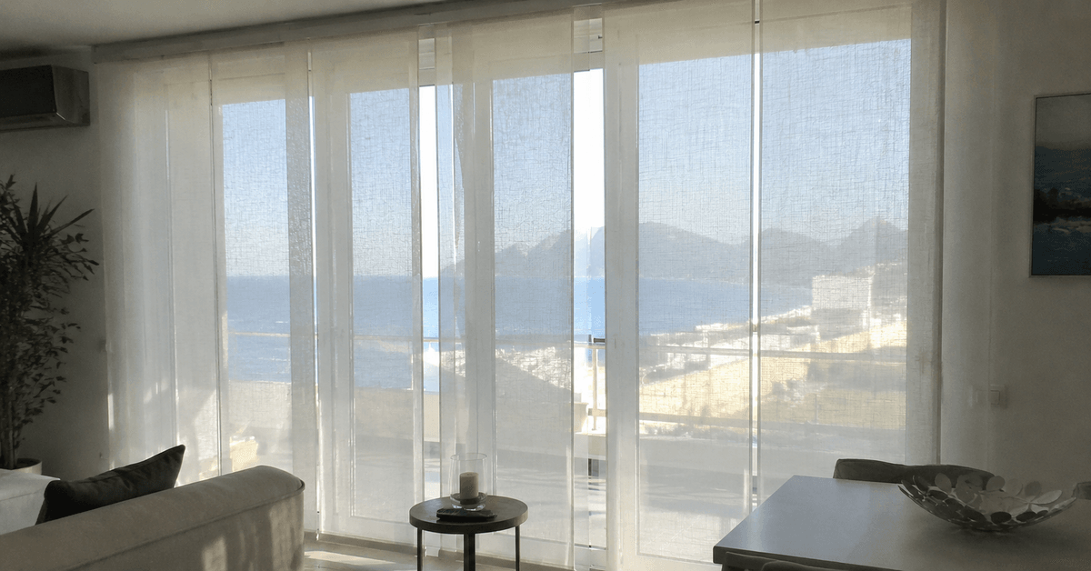 Soggiorno con grande vetrata a sud schermata da tende tecniche filtranti, luce ammorbidita e vista esterna percepibile