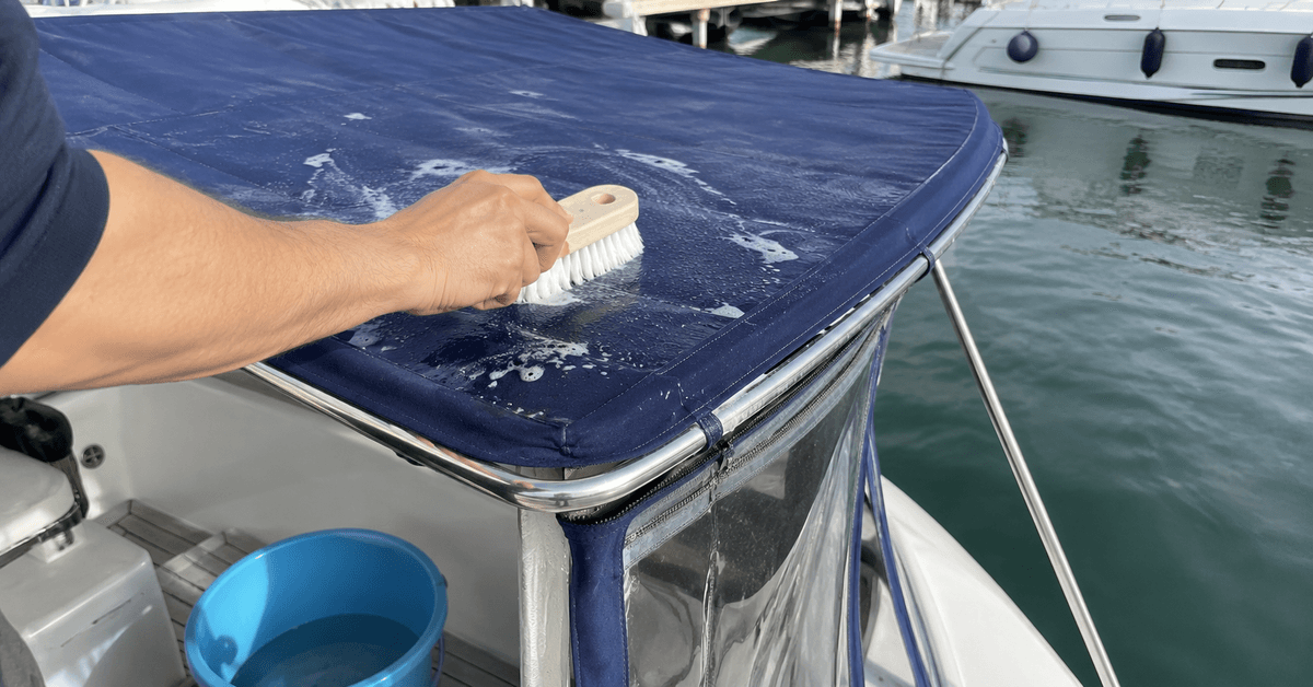 Mani che spazzolano con setole morbide un tendalino acrilico blu di una barca ormeggiata