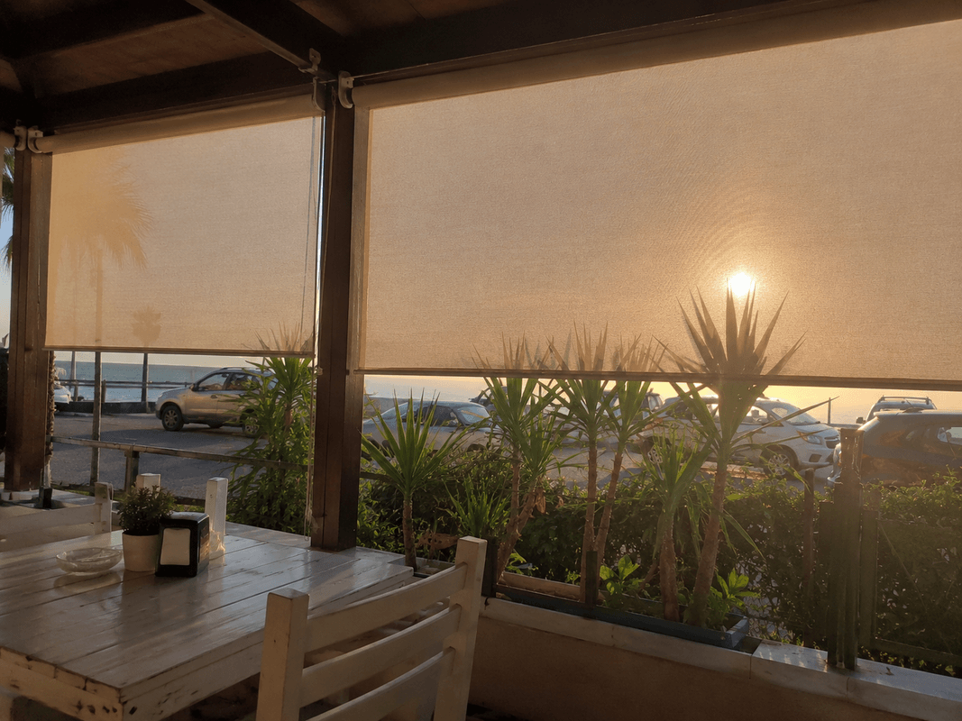 Veranda con tende a rullo in tessuto screen abbassate a metà mentre filtra il sole caldo del tramonto
