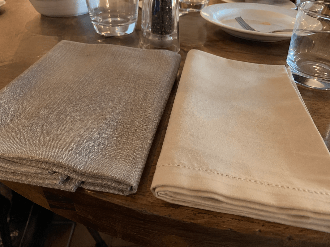 Pila di tovaglioli in tessuto piegati su un tavolo apparecchiato di ristorante in tinte naturali
