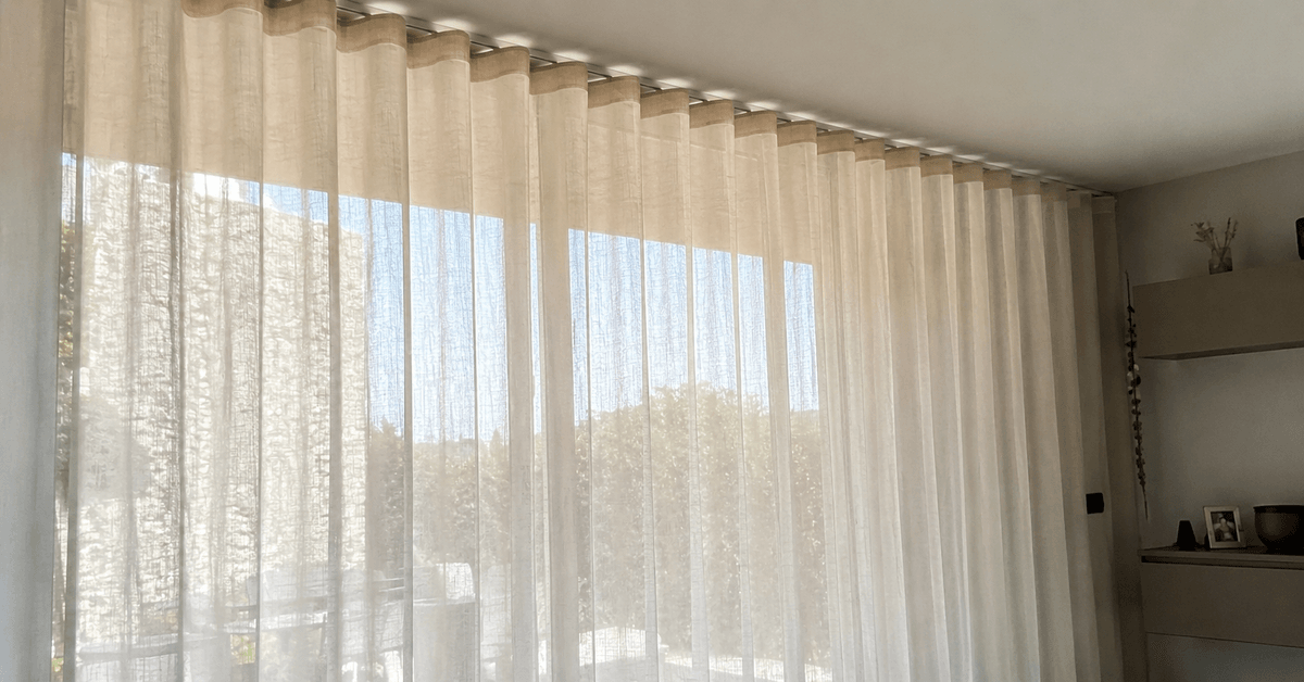 Tenda a onda chiara su binario a soffitto davanti a una vetrata ampia, pieghe morbide e regolari