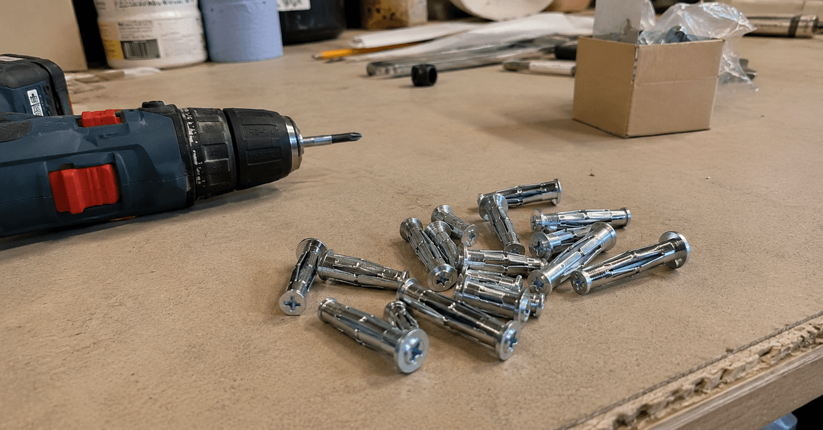 Mani che fissano la staffa di un bastone per tende su una parete in cartongesso con avvitatore e tasselli metallici a espansione