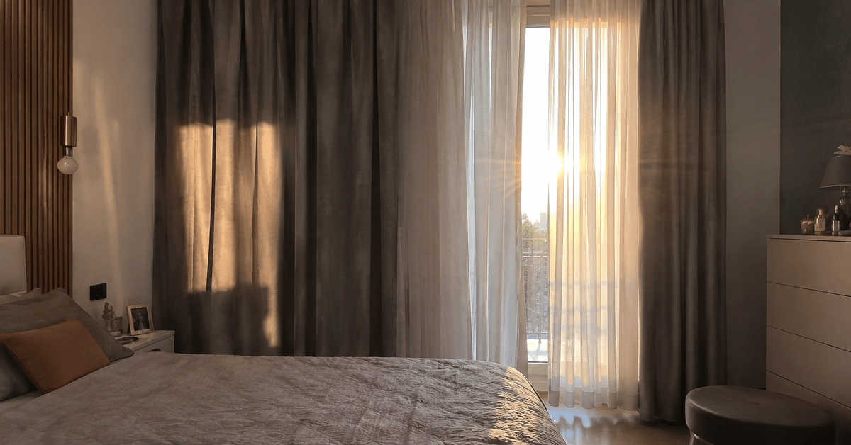 Camera da letto con tende a doppio strato oscurante e filtrante mentre il sole del mattino entra di taglio dalla finestra esposta a est