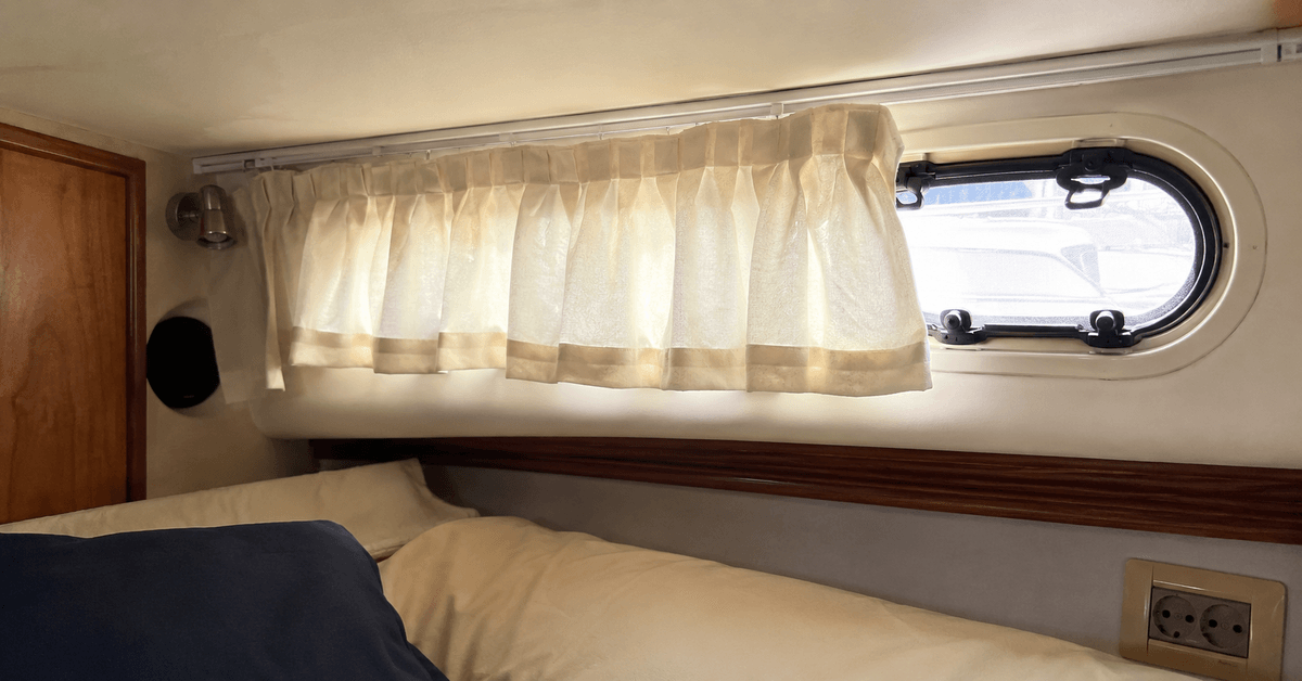 Interno di una cabina di barca con tendina su misura all'oblò semichiusa e luce del mattino che filtra