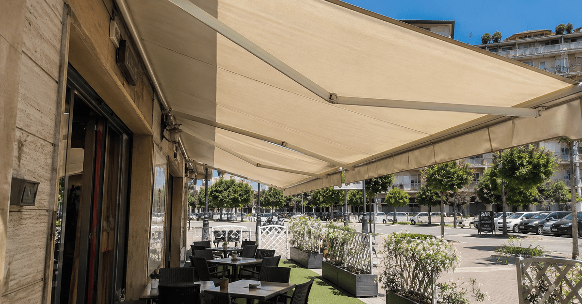 Tenda da sole con telo acrilico ben inclinato aperta sopra il dehor di un bar in una giornata di sole