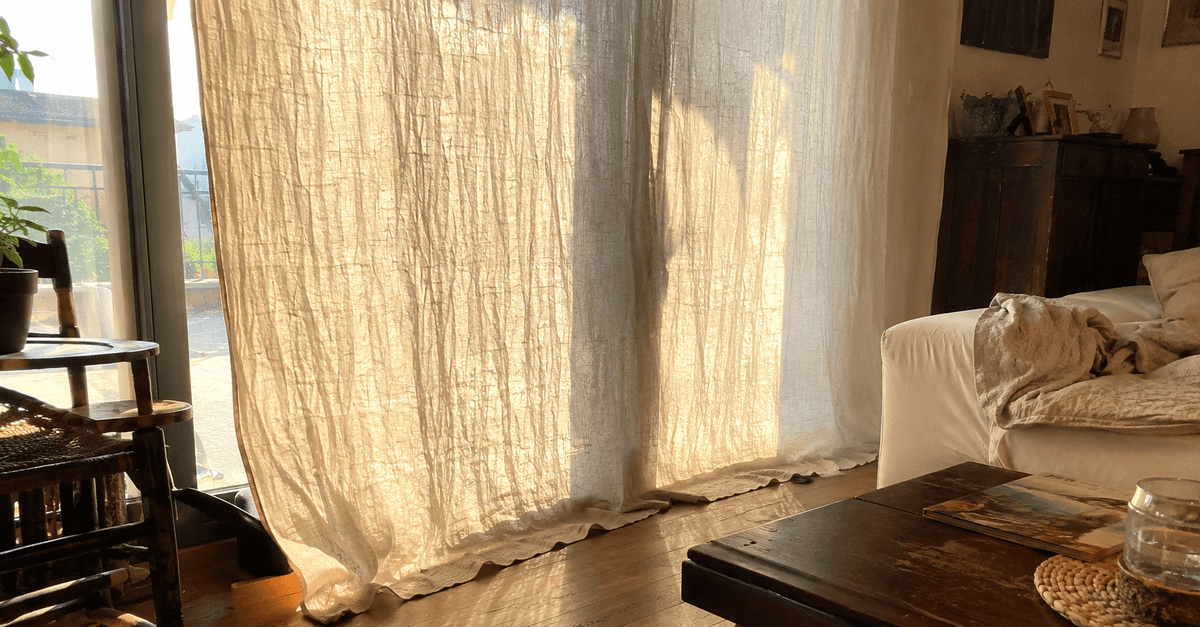 Tenda in lino stropicciato color écru che cade lunga fino al pavimento con la trama irregolare in evidenza