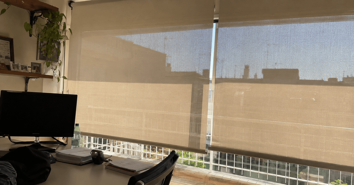 Ufficio con tende a rullo in tessuto screen su una vetrata soleggiata e monitor senza riflessi
