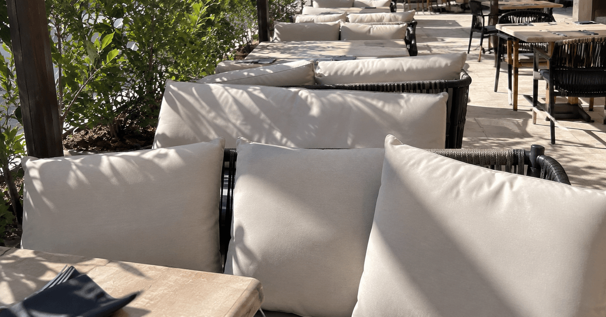 Sedute e cuscini di un dehor di ristorante in tessuto outdoor chiaro sotto il sole estivo