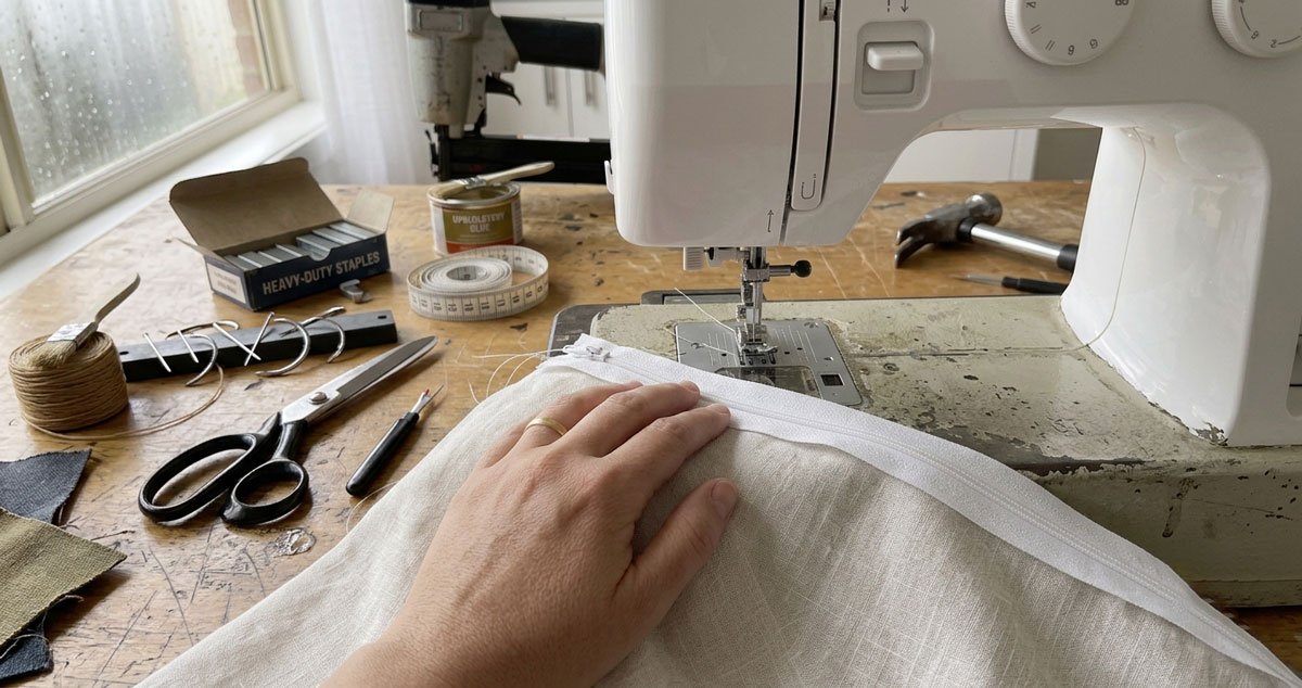 Mani che cuciono alla macchina la fodera di un cuscino con la cerniera su tessuto neutro, tutorial di cucito passo per passo
