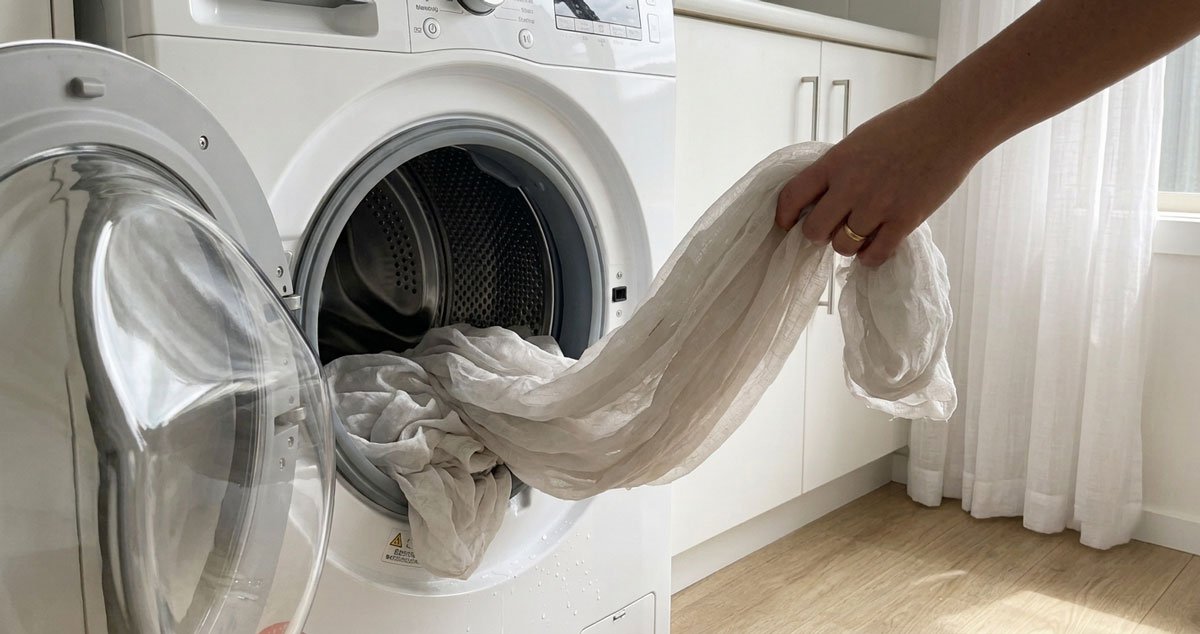 Tende sintetiche chiare in poliestere che entrano in lavatrice con un sacchetto cattura-microfibre, esempio di lavaggio consapevole per ridurre le microplastiche