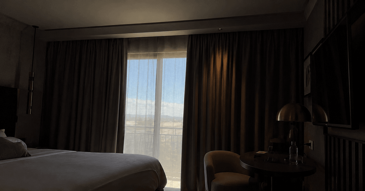 Camera d'hotel con tende blackout ampie che coprono la finestra fino ai lati e in alto, interno in penombra