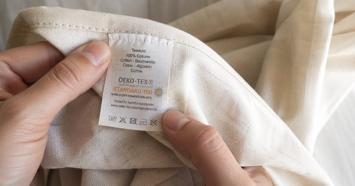 Mani che controllano il cartellino di certificazione GOTS su un tessuto di cotone biologico chiaro
