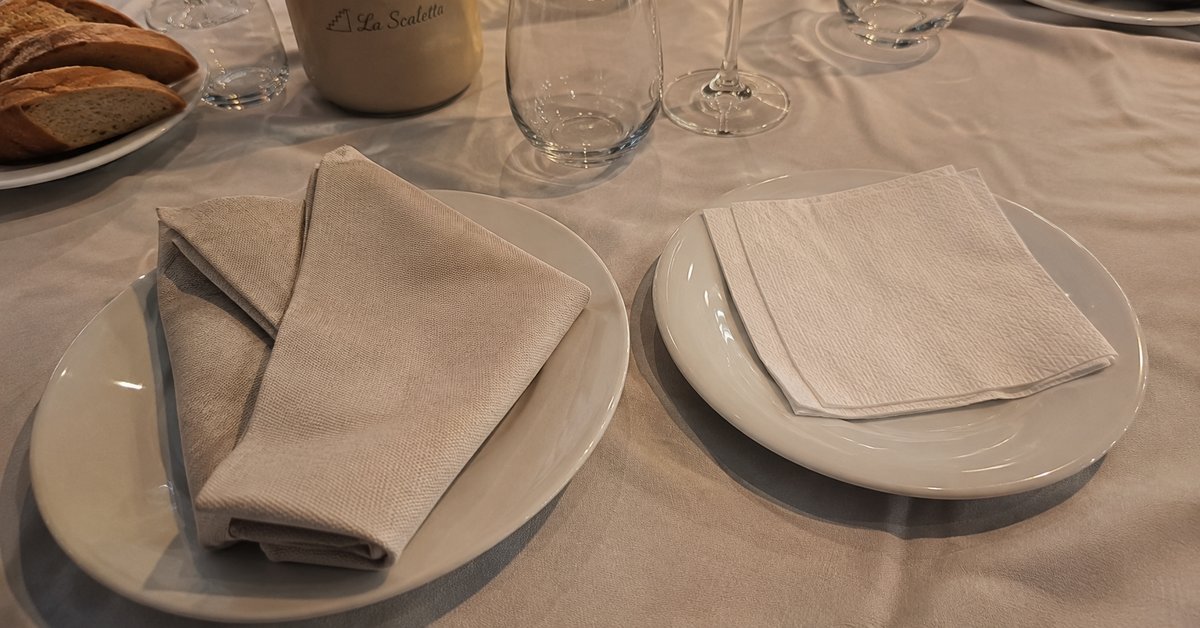 Confronto su un tavolo di ristorante tra un tovagliolo in tessuto piegato con eleganza e uno in carta, mise en place curata