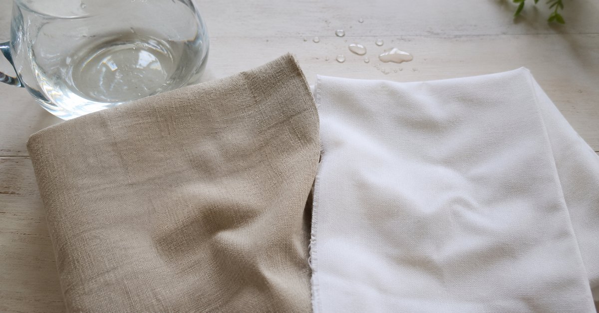 Campioni di tessuto in lino grezzo e cotone bianco affiancati con gocce d'acqua