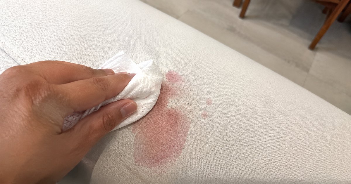 Mano che tampona una macchia di vino rosso su una tovaglia chiara con un panno bianco