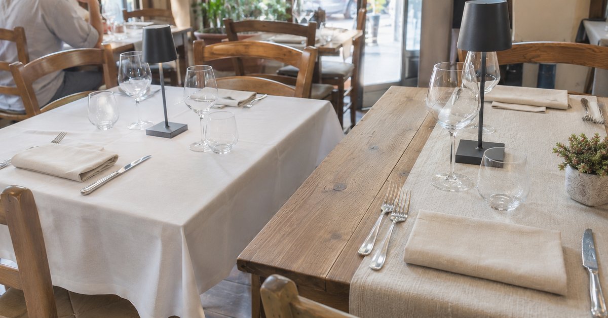 Due tavoli di ristorante a confronto, uno con tovaglia bianca intera e uno con runner centrale