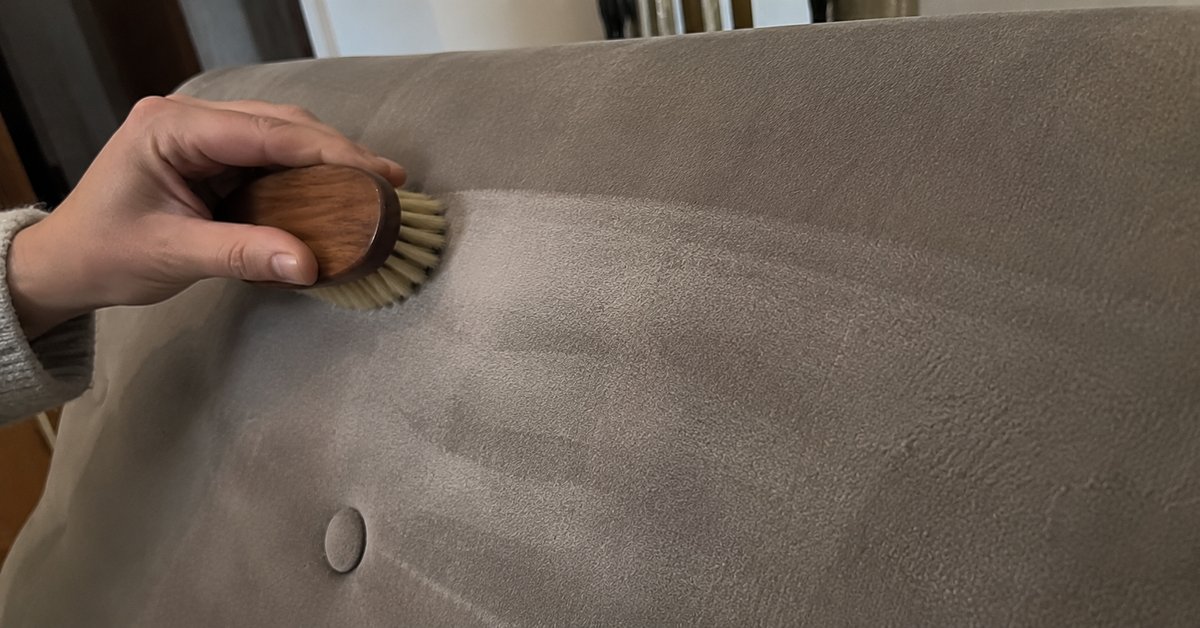 Mani che spazzolano delicatamente nel verso del pelo il velluto di una poltrona con una spazzola morbida