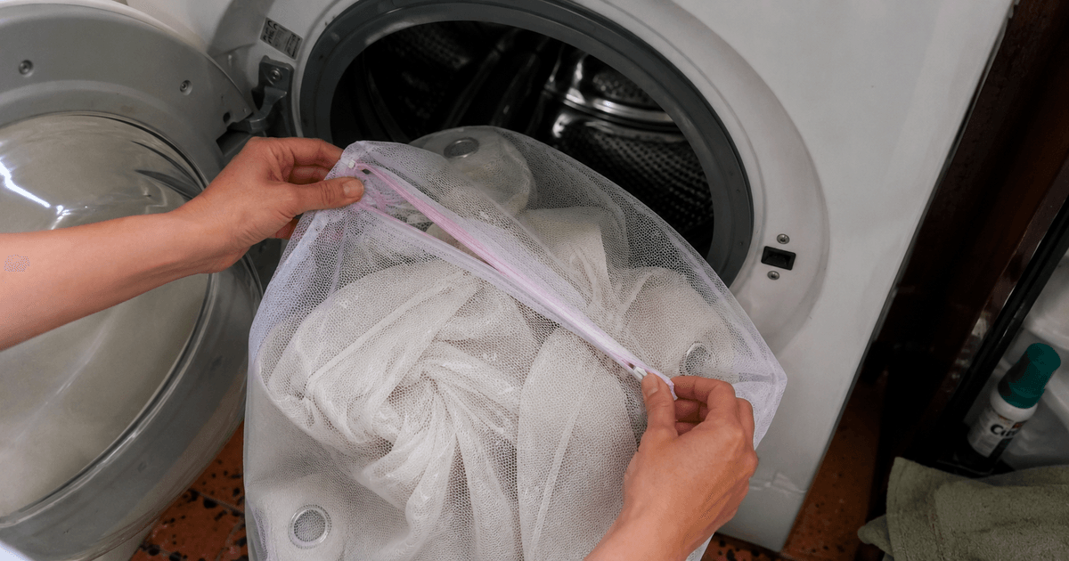 Tende sintetiche inserite in un sacchetto per microfibre davanti all'oblò della lavatrice per ridurre le microplastiche nel lavaggio