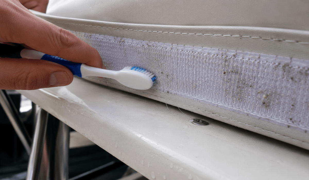 Dettaglio di una striscia di velcro cucita sul bordo di un tendalino nautico, con sale e filacci tra gli uncini, pulita a mano con uno spazzolino