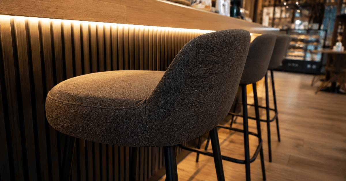 Sgabelli imbottiti con rivestimento scuro resistente allineati al bancone di un bar