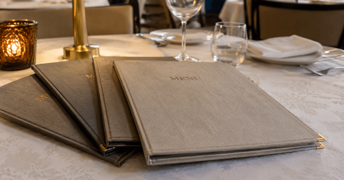 Cartelle porta-menu rivestite a mano in tessuto e similpelle sul tavolo apparecchiato di un ristorante elegante