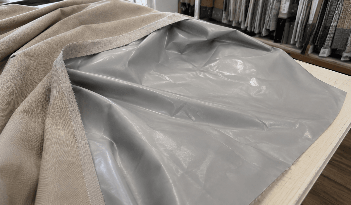 Retro di una tenda oscurante con spalmatura gommata segnato da pieghe da imballo, accanto un vaporizzatore tenuto a distanza