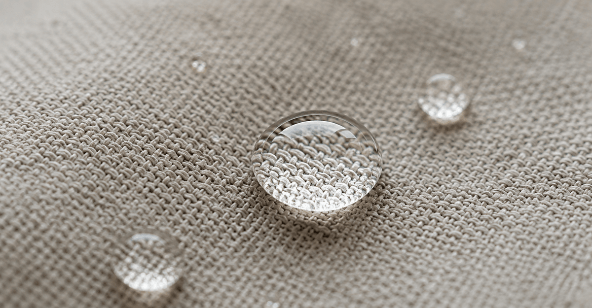 Goccia d'acqua che perla su un tessuto d'arredo idrorepellente senza PFAS in luce naturale