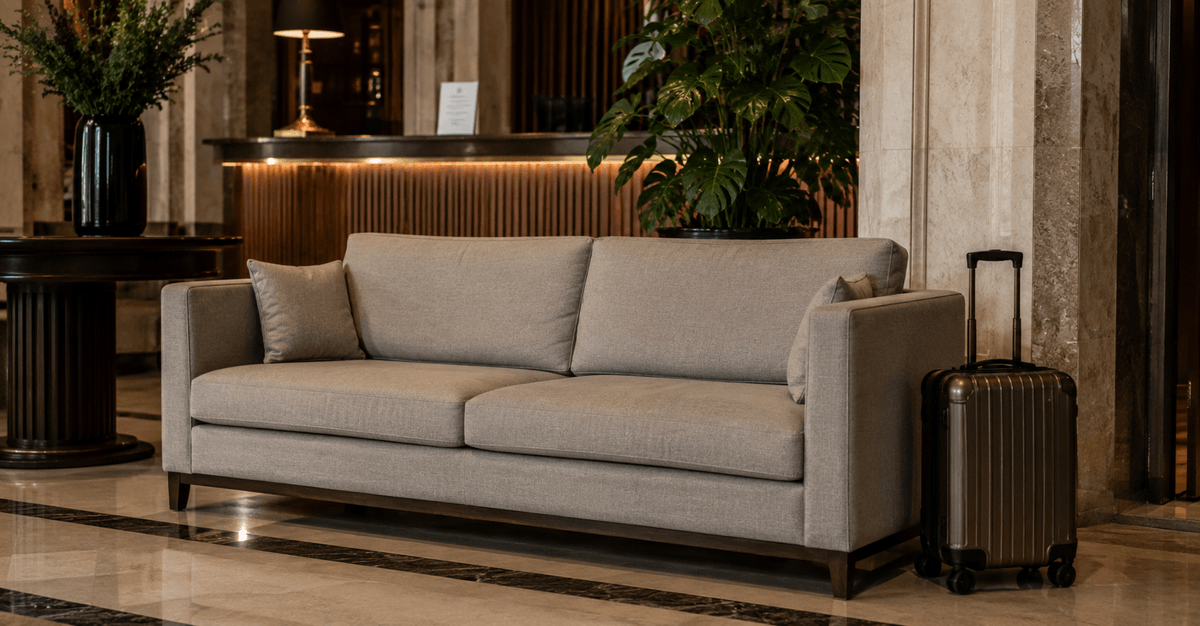Divano robusto nella hall di un hotel con un trolley appoggiato accanto, tessuto contract resistente