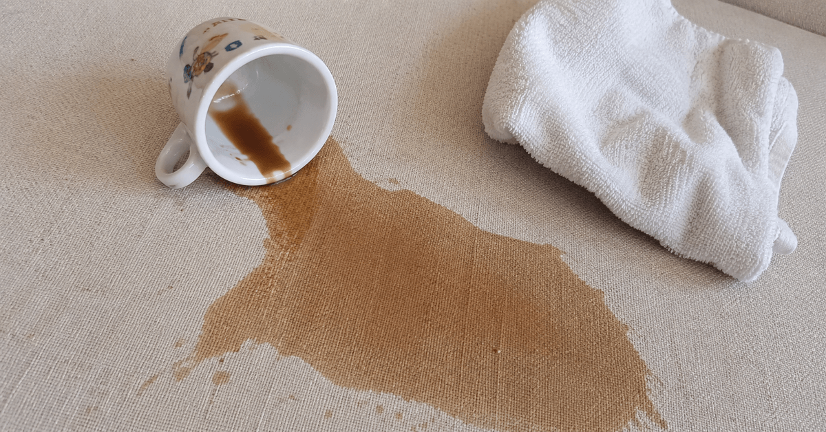 Macchia di caffè su un tessuto d'arredo chiaro con panno pulito accanto