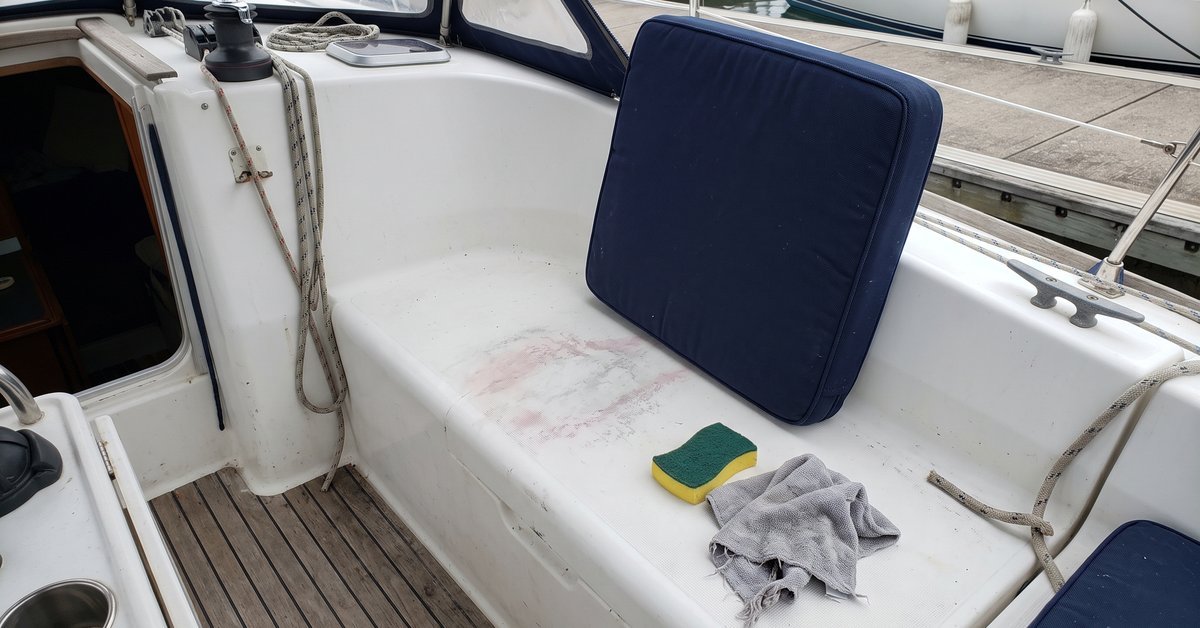 Cuscino nautico di tinta scura sollevato sul pozzetto e alone di colore sul gelcoat bianco della barca