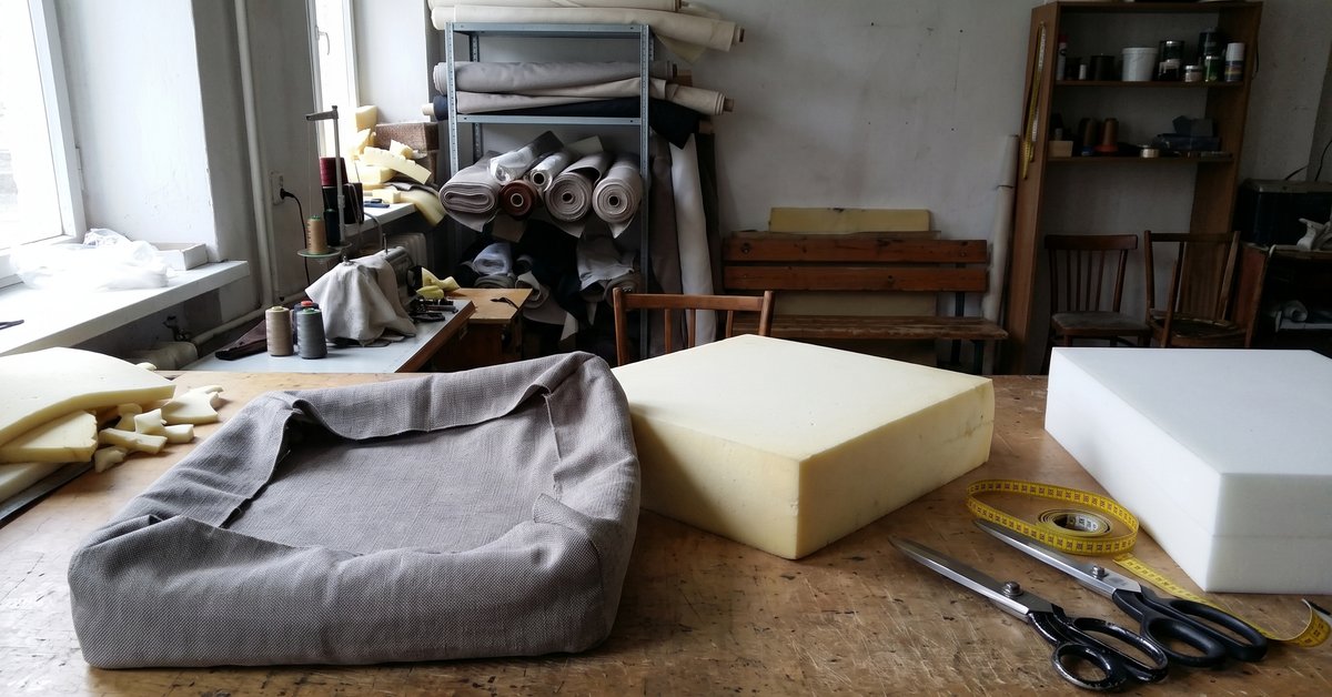 Cuscino del divano sfoderato sul tavolo del tappezziere con l'imbottitura in gommapiuma estratta accanto alla fodera vuota