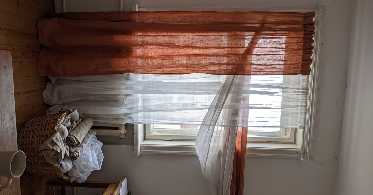 Finestra con doppia tenda, un voile chiaro trasparente davanti e un lino pesante color ruggine dietro su doppio binario