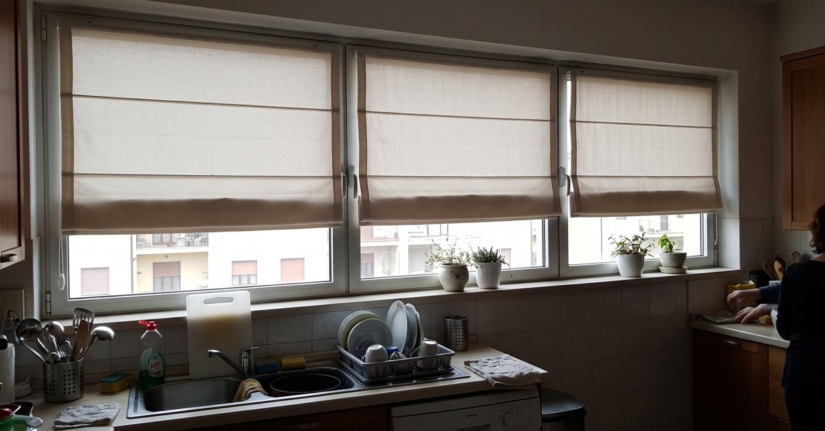 Finestra a nastro orizzontale in cucina moderna vestita con tende a pacchetto chiare affiancate e allineate