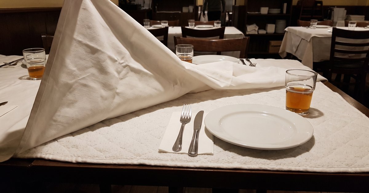 Tavolo di ristorante con la tovaglia bianca sollevata da un angolo che mostra il mollettone imbottito steso sotto sul piano