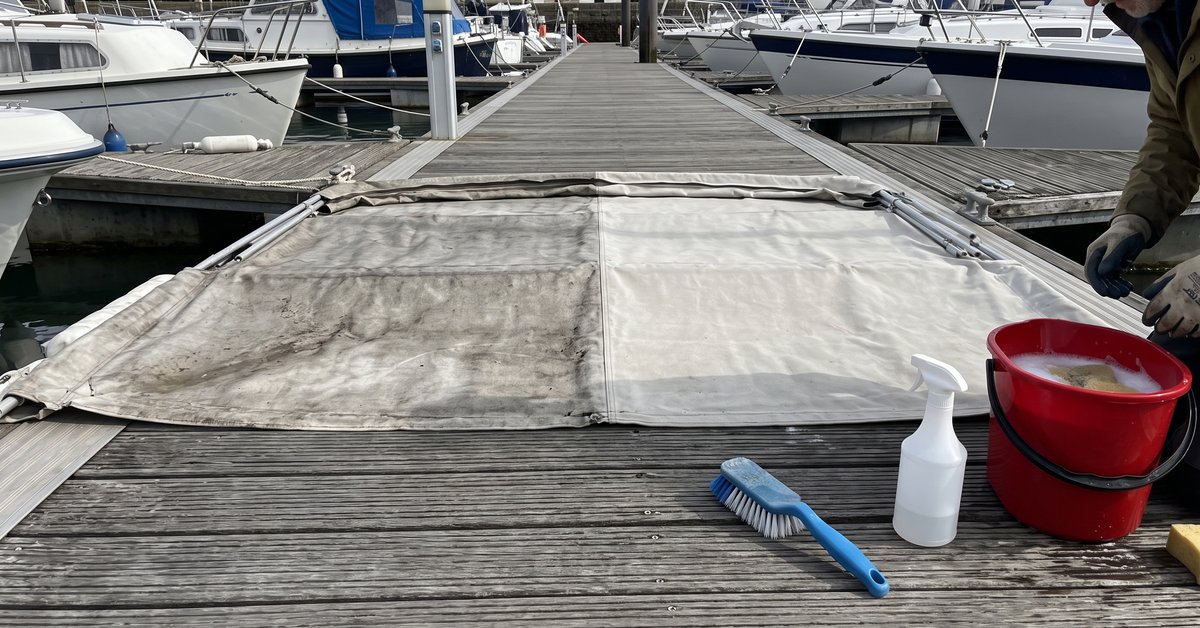 Tendalino bimini steso su un pontile, una metà ancora grigia e una pulita, con spazzola, secchio e spray idrorepellente