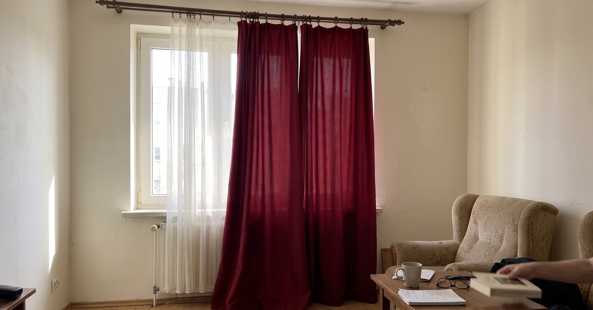 Tende bordeaux in un salotto luminoso con pareti chiare e voile bianca davanti alla finestra