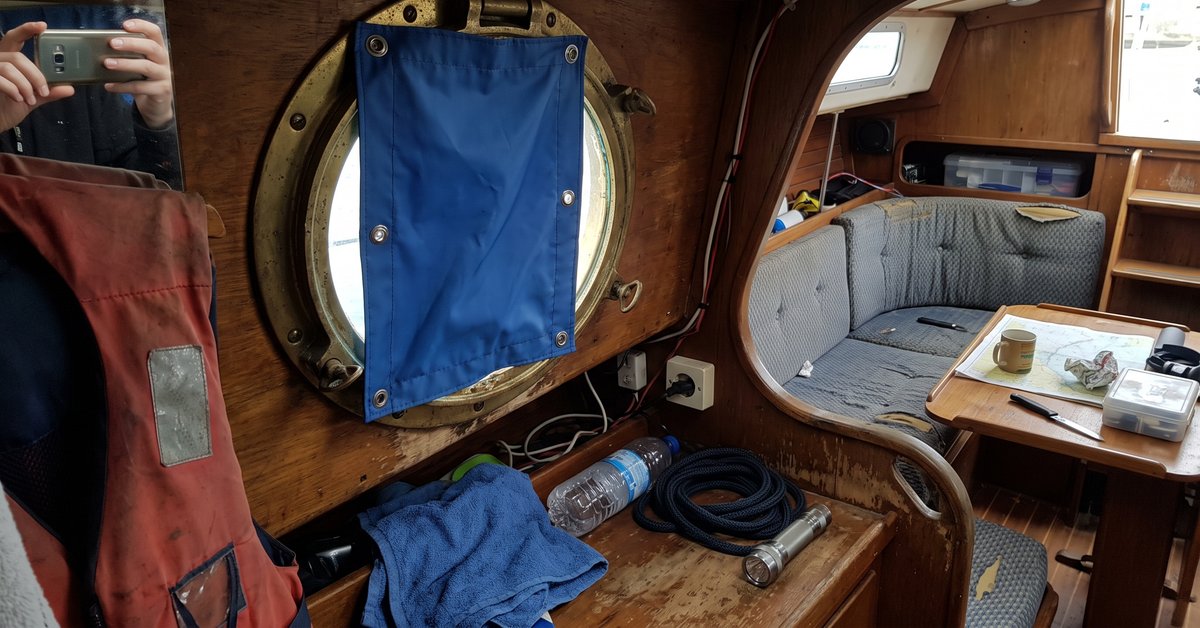 Oblò tondo in ottone nella cabina di una barca a vela con una tendina oscurante in tessuto sintetico blu fissata con bottoni a pressione